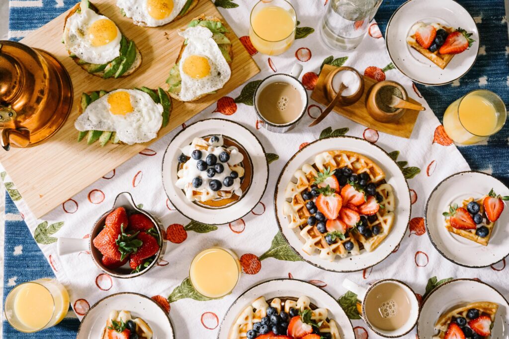 birds eye view of a broker breakfast, one of soul pathology's wellness programs. there are waffles topped with strawberries and blueberries, coffee, orange juice, and avocado egg toast.