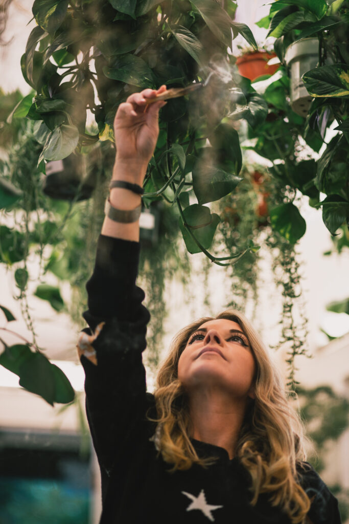 Amanda Rieger Green, a renowned psychic who works with Numerology, is holding sage in the air and looking up at it.